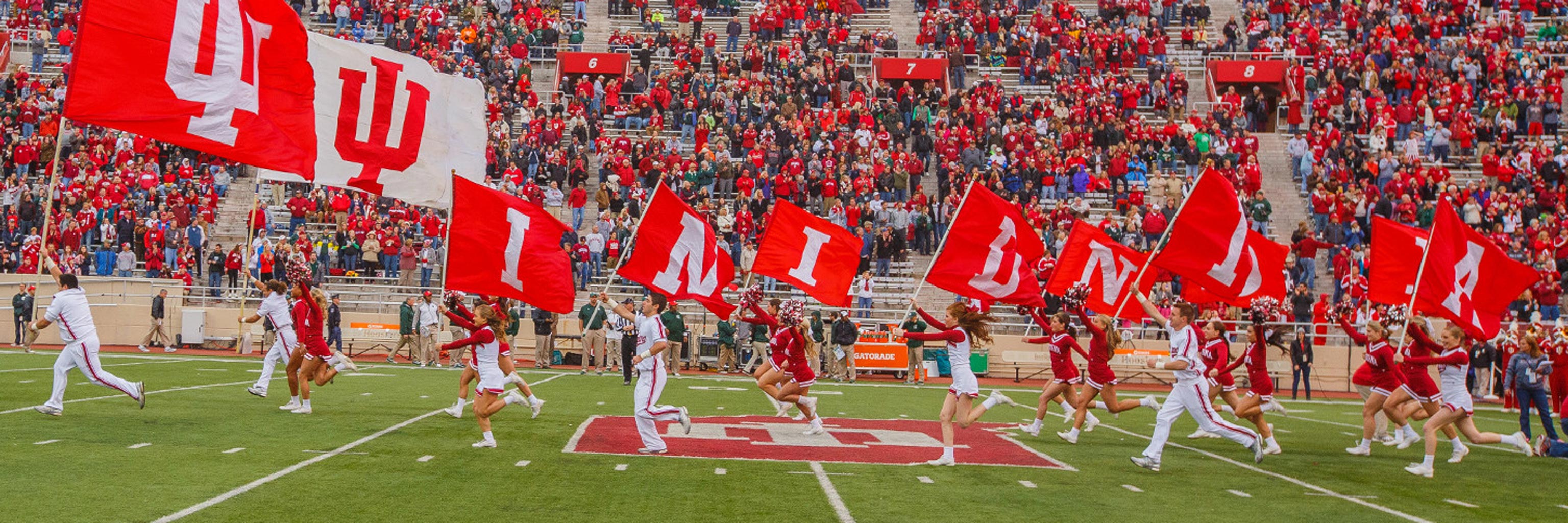 Indiana University cheering team running down football field with school flags