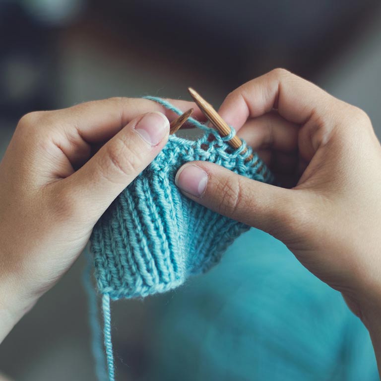 Close up of hands knitting light blue yarn