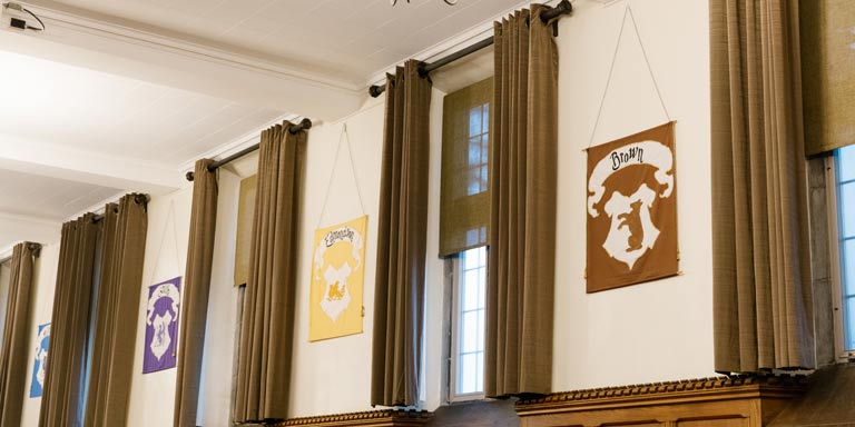 Four posters, each containing a different crest, hang separated by windows in the Collins dining hall