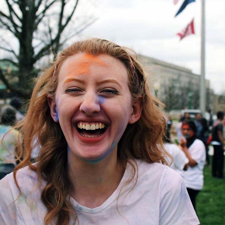 White female student smiling with smears of brightly colored powder on her face