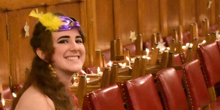 Student with a purple masquerade mask lifted up smiling 